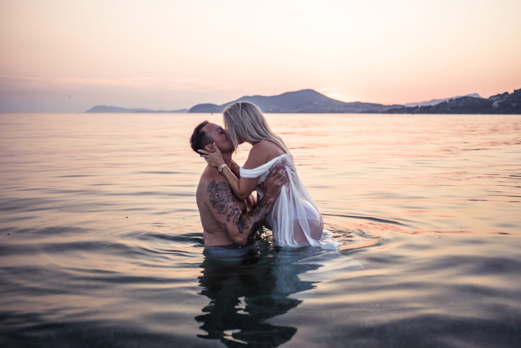 Photo grossesse à Hyères, couple s’embrassant dans l’eau au coucher du soleil
