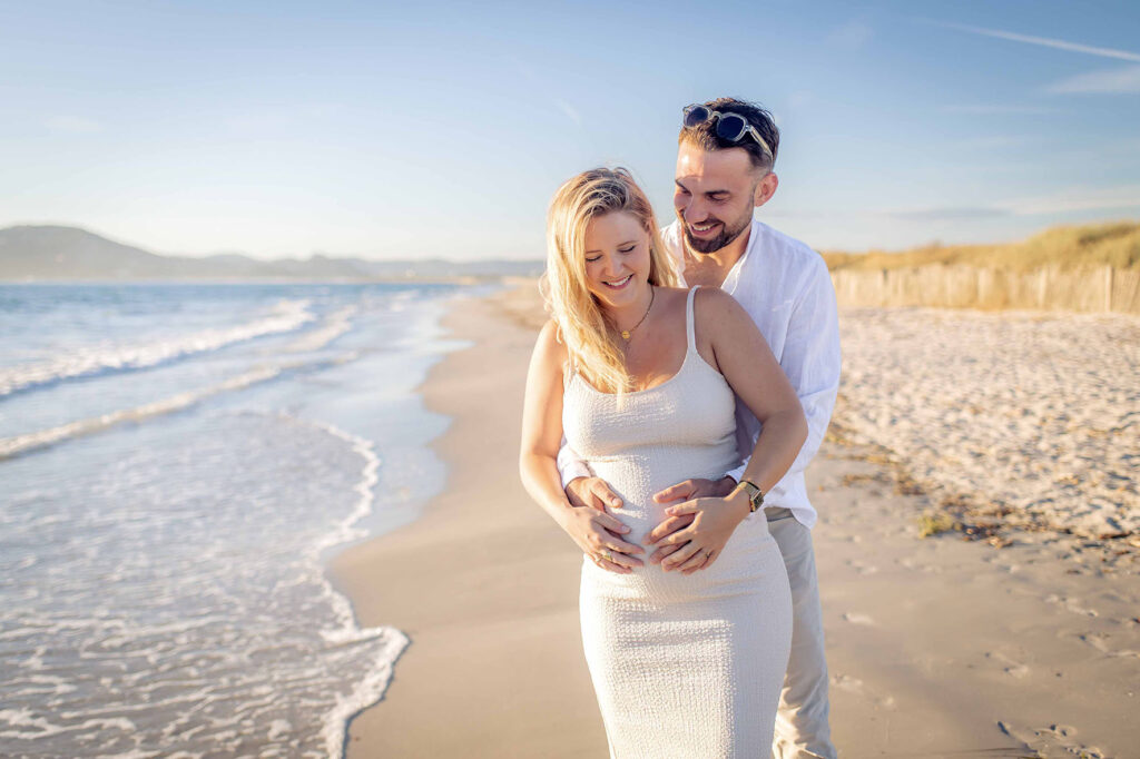 Photo grossesse à Hyères, couple souriant sur la plage au lever du soleil