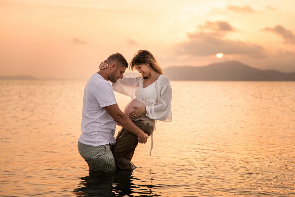 Photo grossesse à Hyères au coucher du soleil, couple dans l’eau en lumière dorée