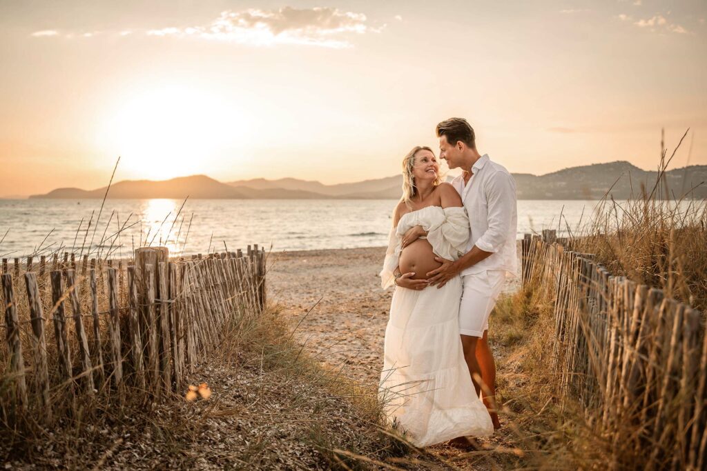 Photo grossesse à Hyères sur la plage au coucher du soleil, couple tendre en robe blanche