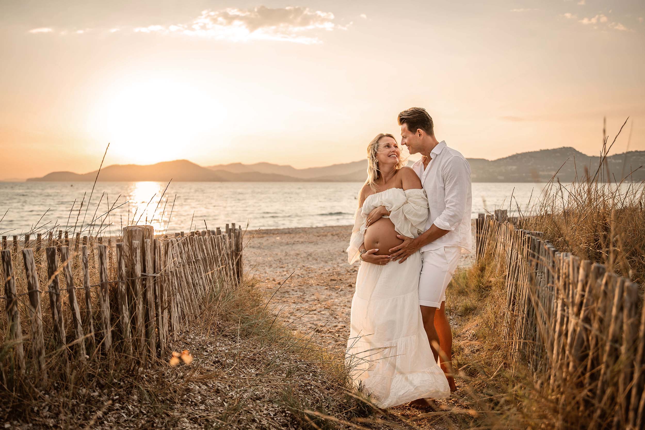 Photo grossesse à Hyères sur la plage au coucher du soleil, couple tendre en robe blanche