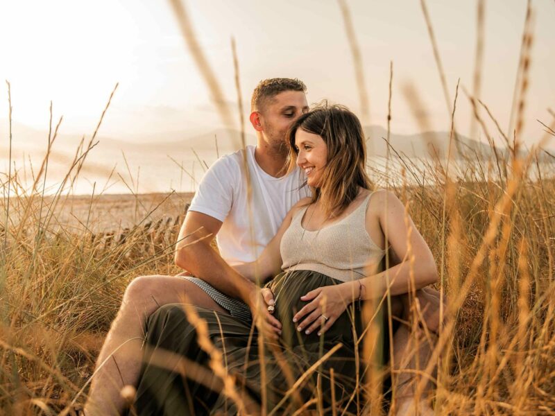 Séance photo grossesse à Hyères, couple assis dans les herbes dorées au coucher du soleil