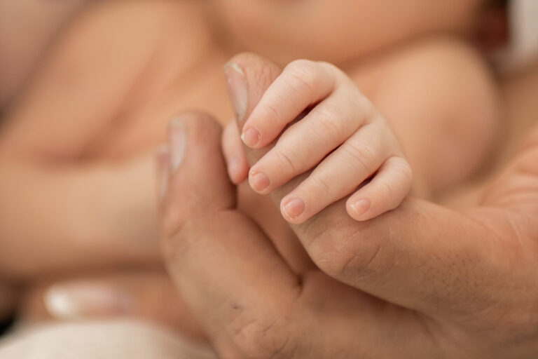 Détail des mains d’un nouveau-né tenant le doigt de son parent lors d’une séance photo naissance lifestyle à domicile à Hyères