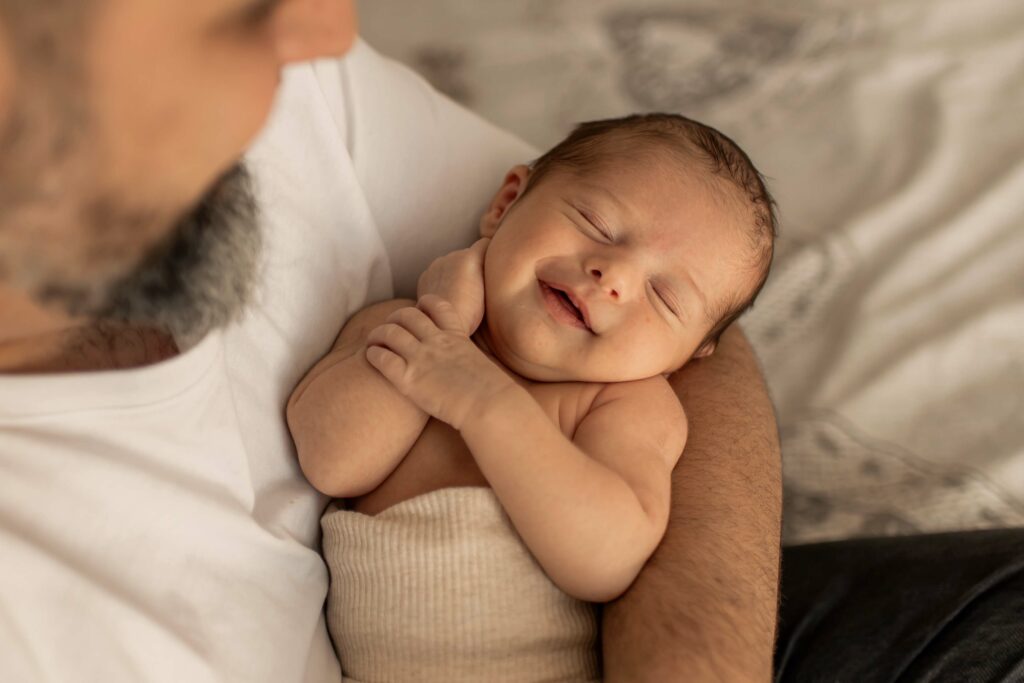 Nouveau-né endormi dans les bras de son papa pendant une séance photo naissance lifestyle à domicile à Hyères
