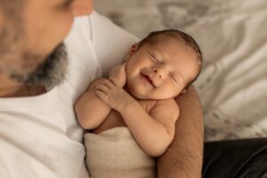 Nouveau-né endormi dans les bras de son papa pendant une séance photo naissance lifestyle à domicile à Hyères
